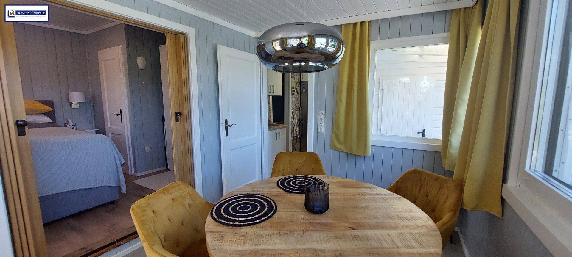Essbereich mit Holztisch und Blick in ein angrenzendes Schlafzimmer, helle und freundliche Atmosphäre.