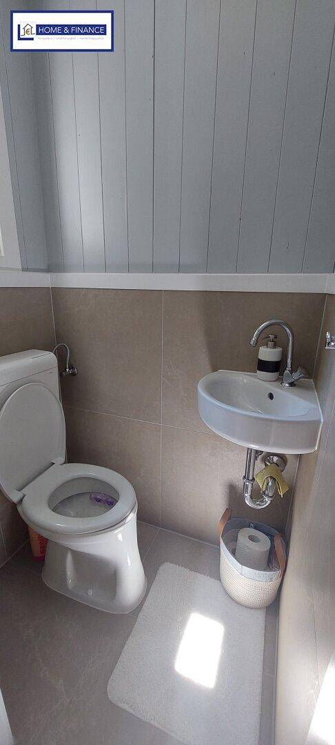 Kleines Gäste-WC mit Toilette und Eckwaschbecken, geflieste Wände und Boden.