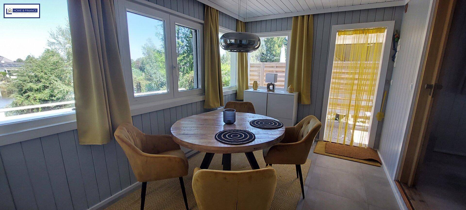 Gemütlicher Essbereich mit Holztisch und gelben Stühlen, Zugang zur Terrasse durch eine Tür mit Vorhang.