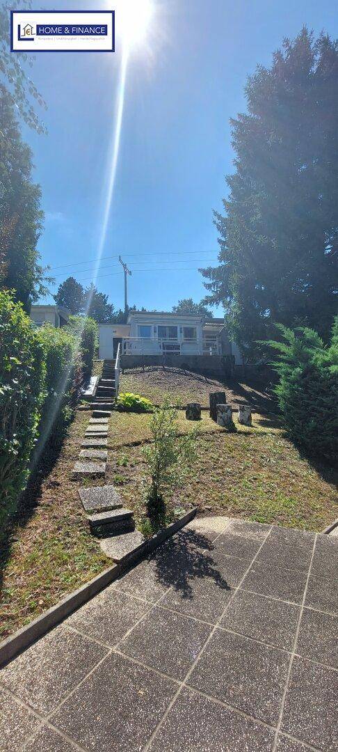 Außenansicht des Hauses vom Gartenbereich aus, mit Hanglage und umgebenden Bäumen.