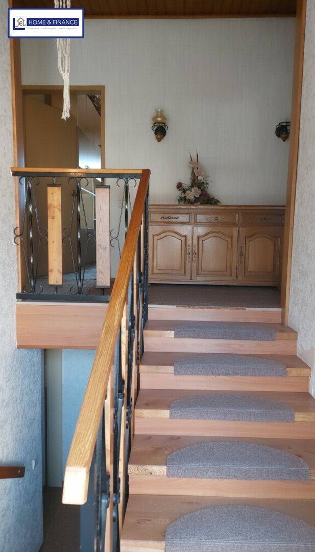 Treppenaufgang mit Holzstufen und Teppichläufern, führt zu einem Flur mit Holzmöbeln.