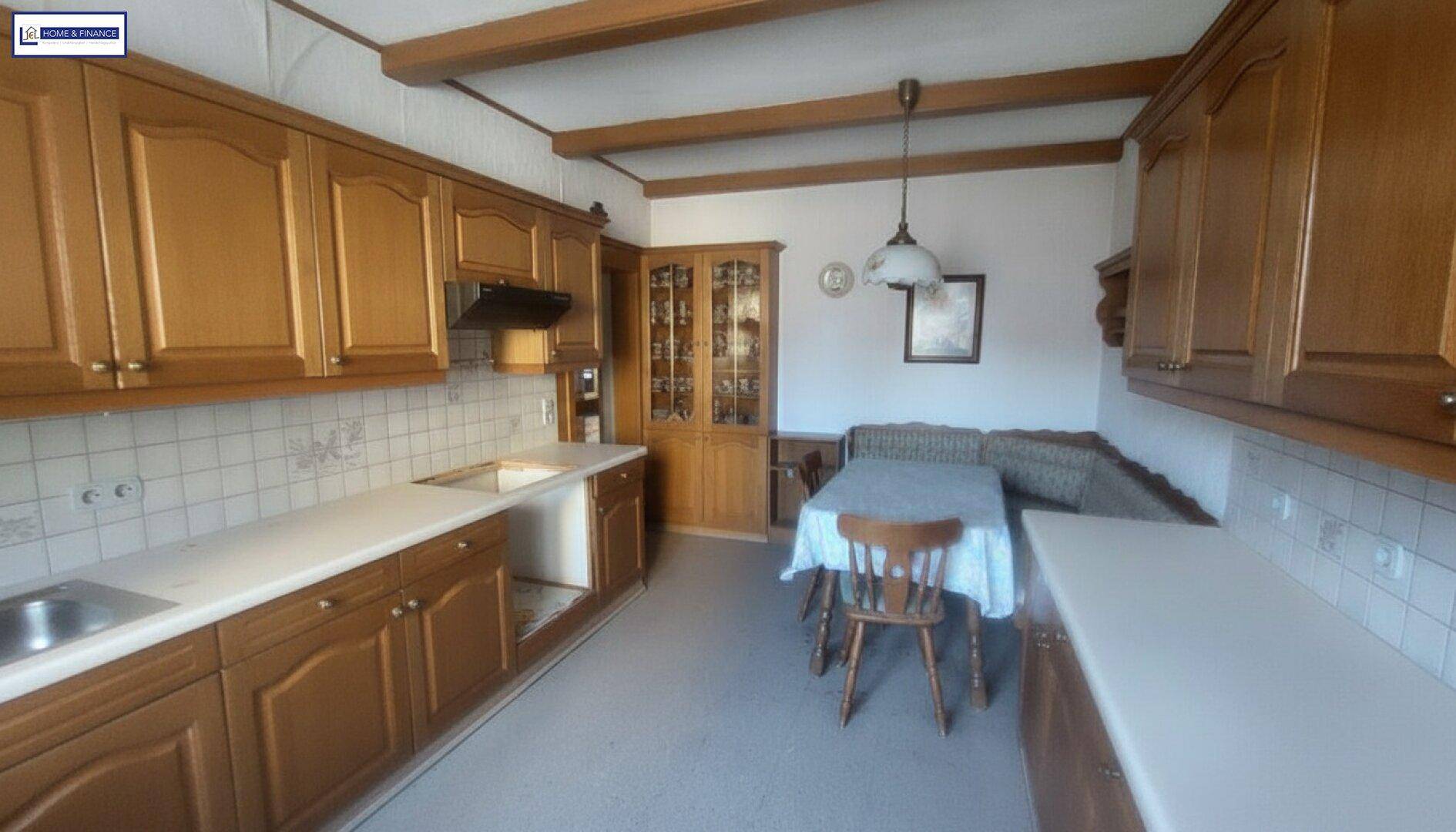 Traditionelle Küche mit Holzschränken, Essbereich und sichtbaren Deckenbalken.