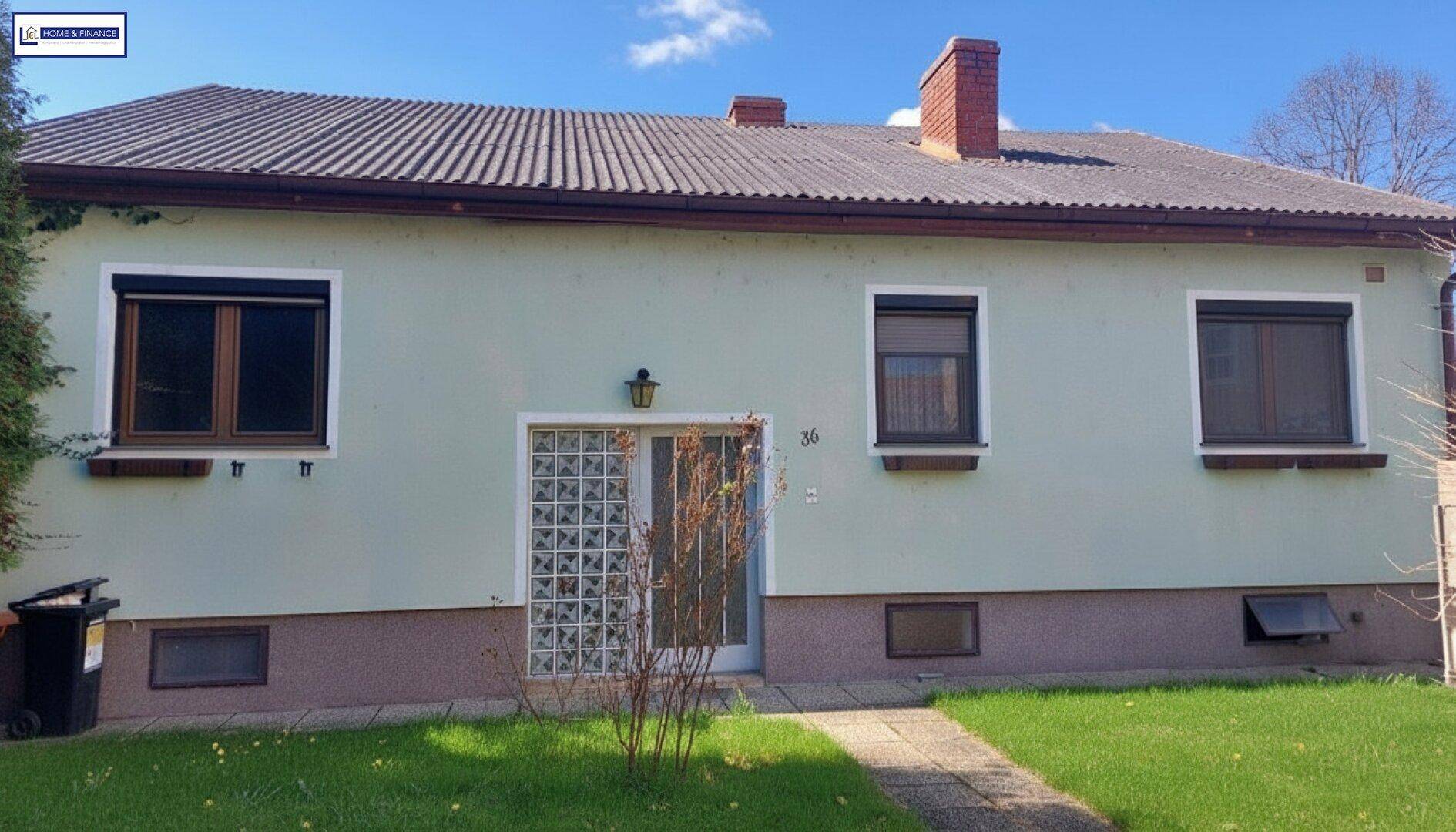 Rückseite des Einfamilienhauses mit hellgrüner Fassade, Rollläden und Kamin auf dem Dach.