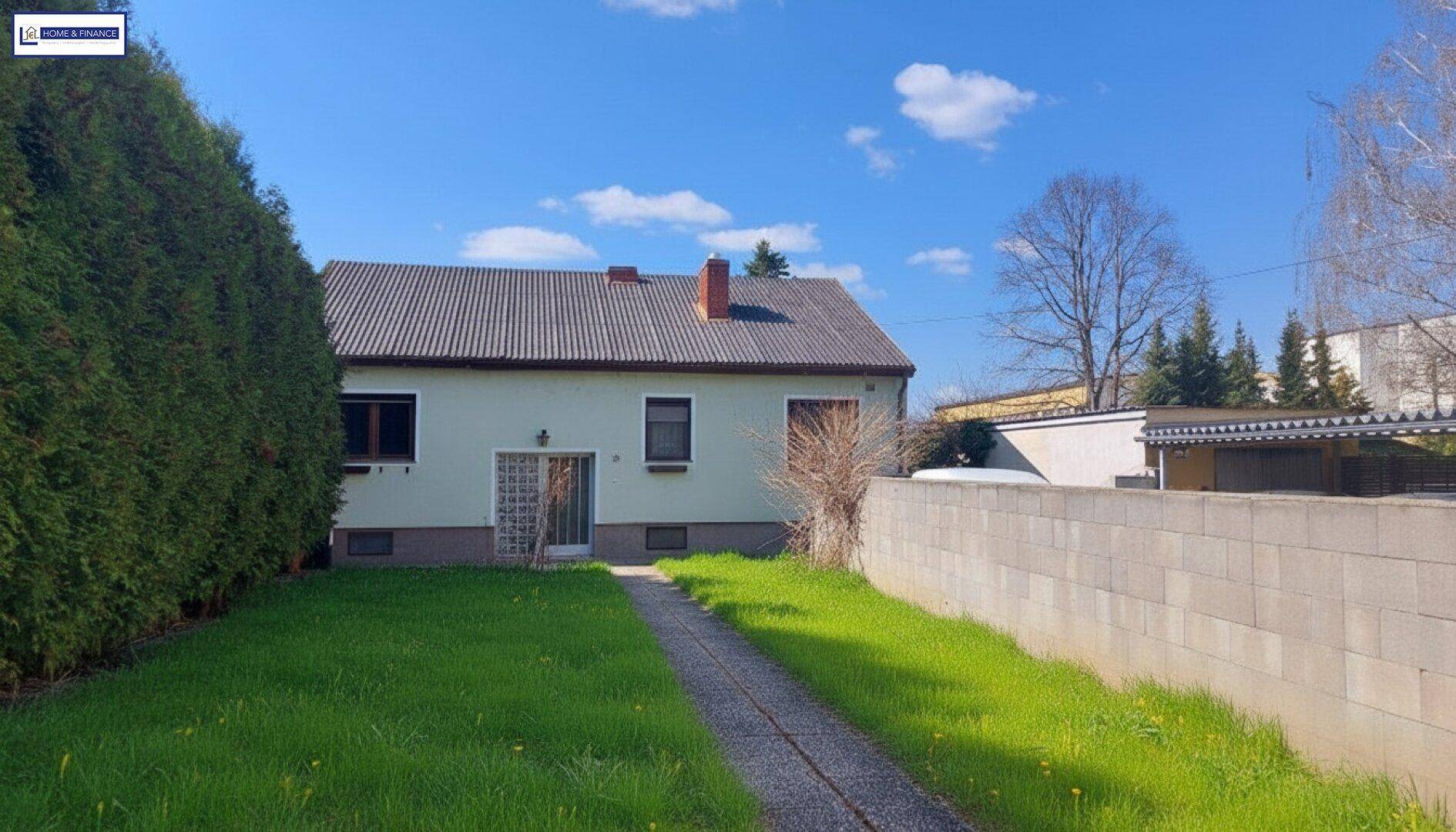 Seitenansicht des Hauses mit gepflegtem Rasen, hoher Hecke und Zufahrtsweg.