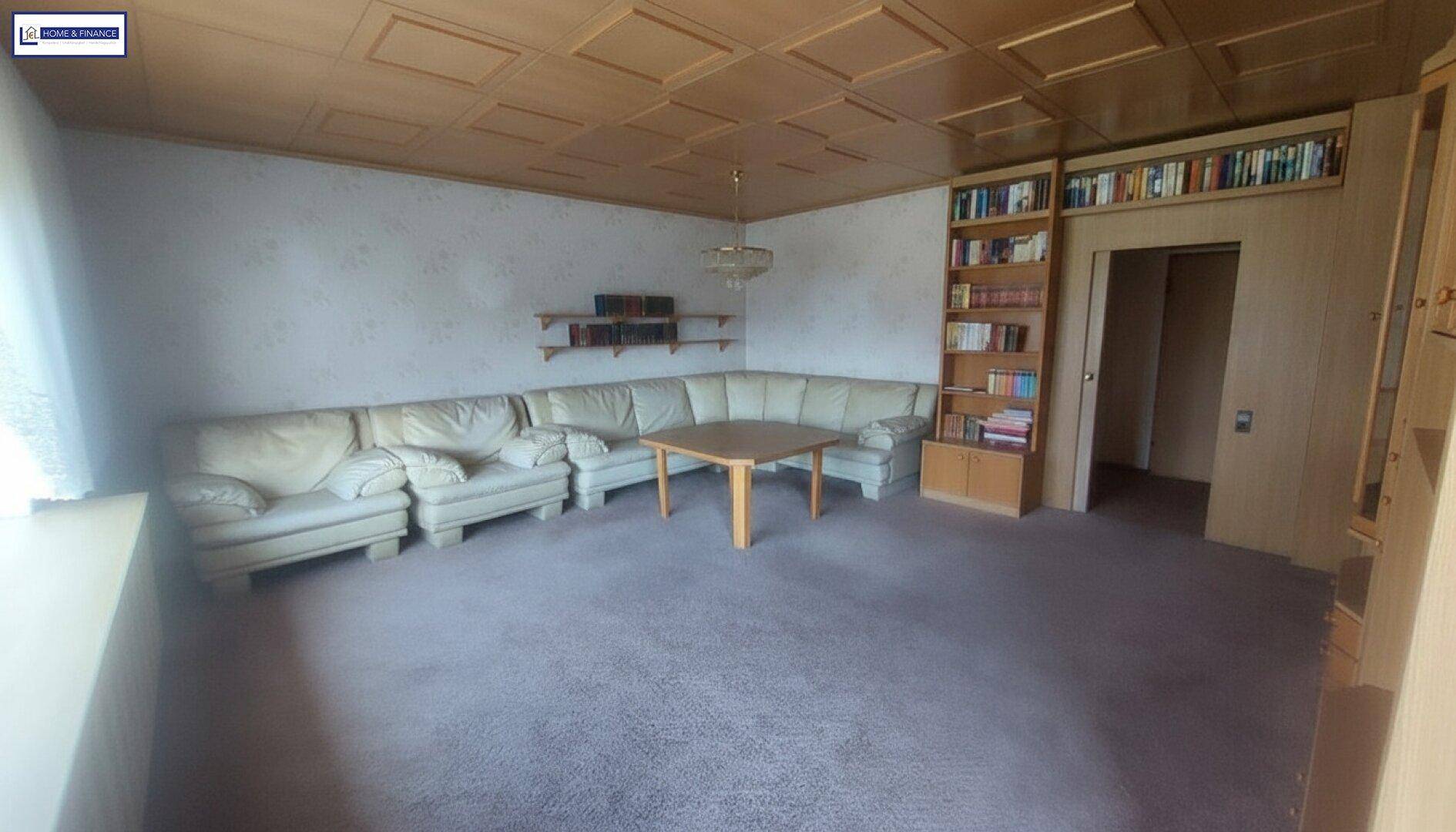 Geräumiges Wohnzimmer mit Teppichboden, großer Eckcouch und Holzpaneeldecke.