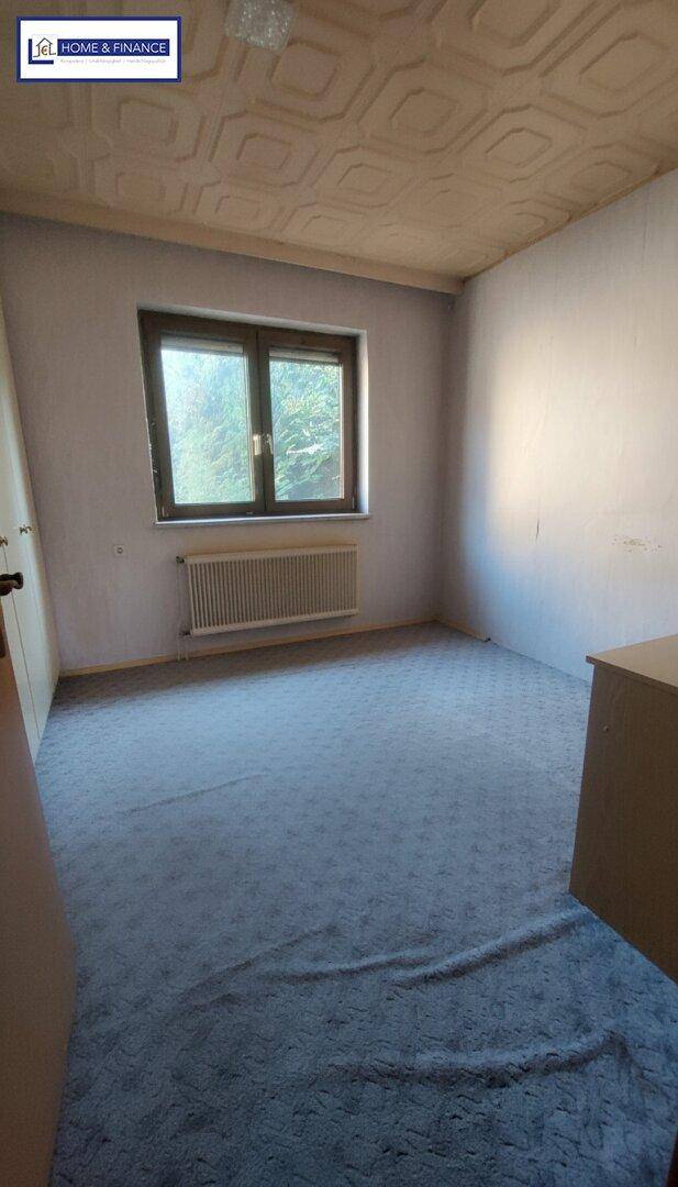 Helles Schlafzimmer mit grauem Teppichboden, Fenster und Heizkörper unter dem Fenster.