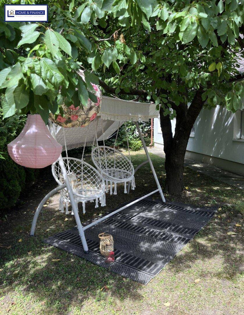 Gemütlicher Sitzbereich im Garten mit Hängesesseln und dekorativen Laternen unter einem Baum.