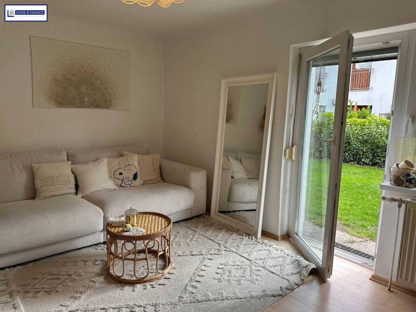 Helles Wohnzimmer mit beigem Sofa, Teppich und direktem Zugang zum grünen Garten.