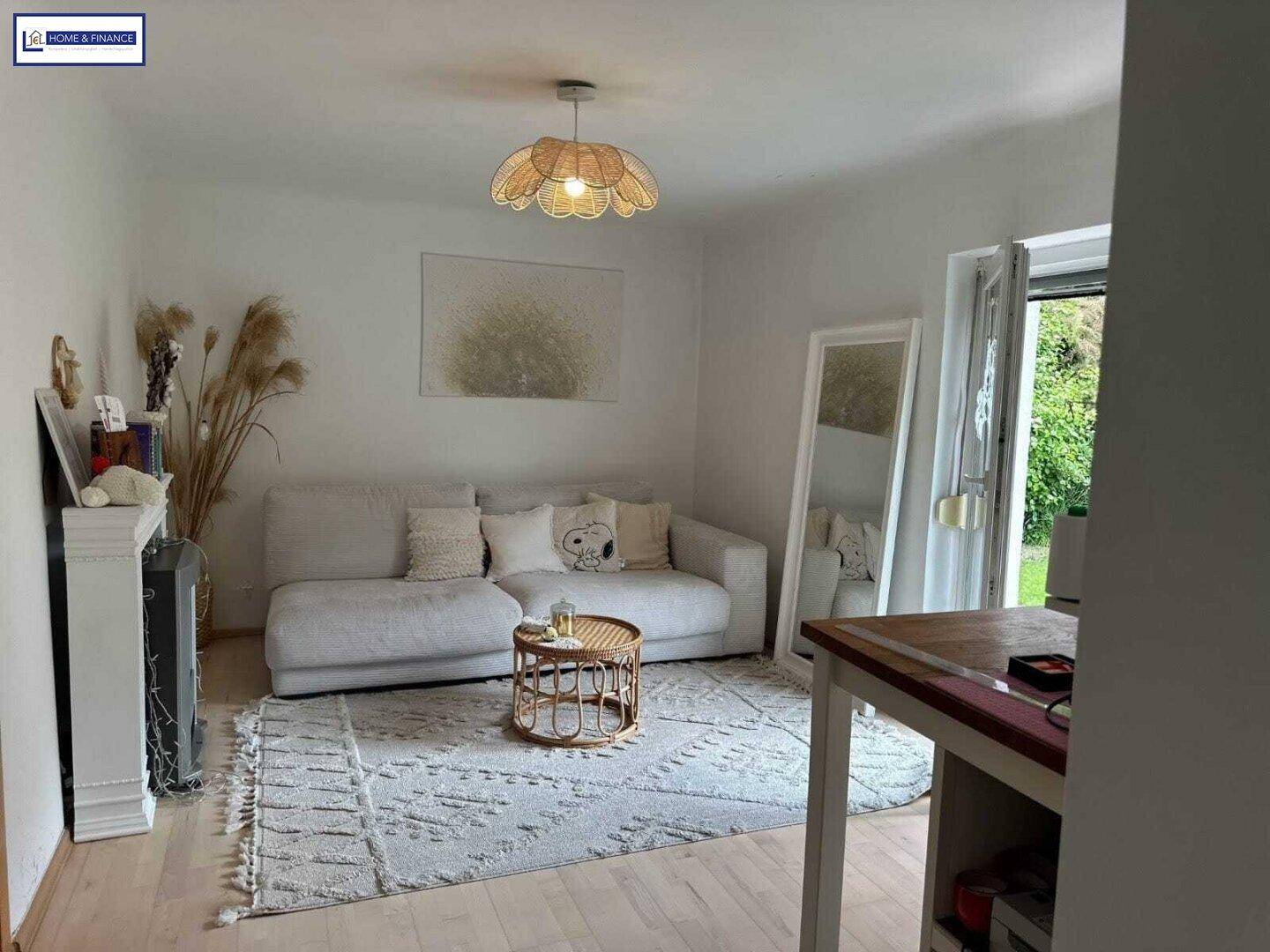 Geräumiges Wohnzimmer mit hellem Sofa, dekorativem Teppich und Zugang zum Außenbereich.