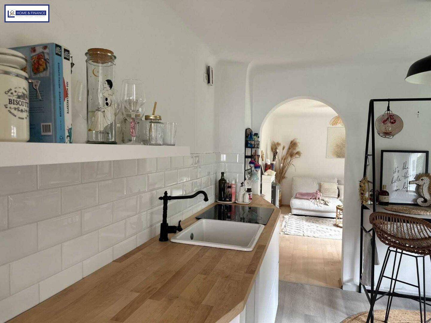 Moderne Küche mit Holz-Arbeitsplatte, Induktionskochfeld und offenem Durchgang zum Wohnbereich.