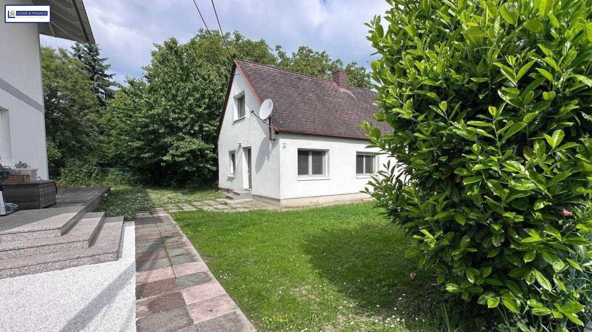 Freistehendes Haus mit weißer Fassade, umgeben von Rasenflächen und Bäumen.
