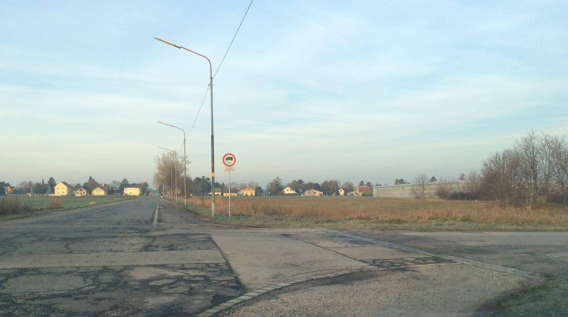 Kreuzung von Asphaltstraßen mit Straßenlaternen und Häusern in der Ferne unter klarem Himmel.