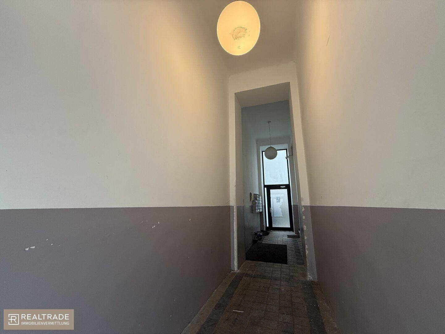 Einfacher Eingangsbereich mit zweifarbigen Wänden und Fliesenboden, führt zum Treppenhaus.