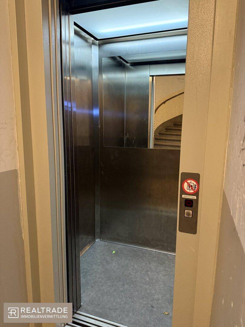 Moderner Aufzug mit Edelstahloberflächen und Blick auf das historische Treppenhaus.