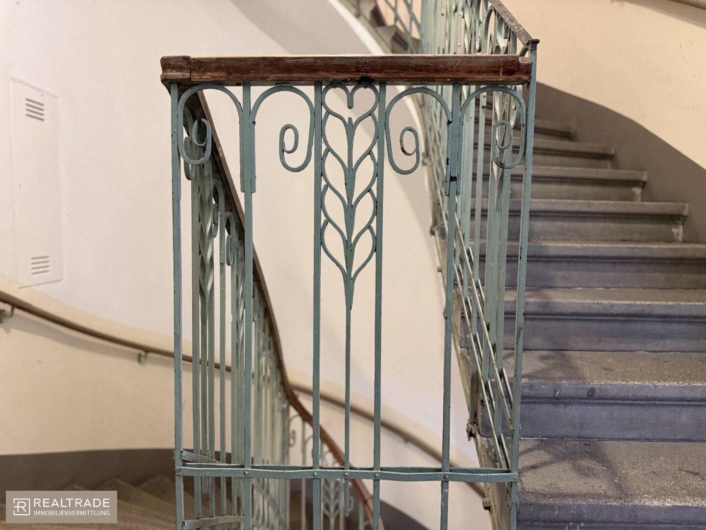 Detailansicht eines historischen Treppengeländers mit kunstvollen Verzierungen und Holzhandlauf.