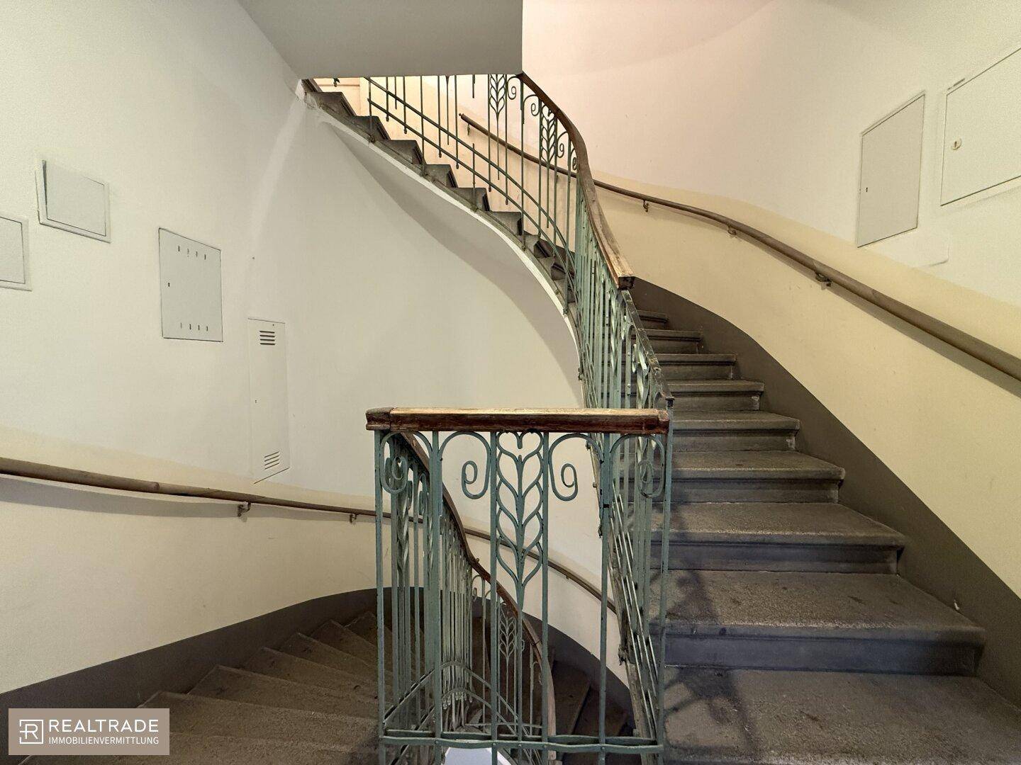 Geschwungenes Treppenhaus mit historischem Geländer und Steinstufen in einem Altbau.