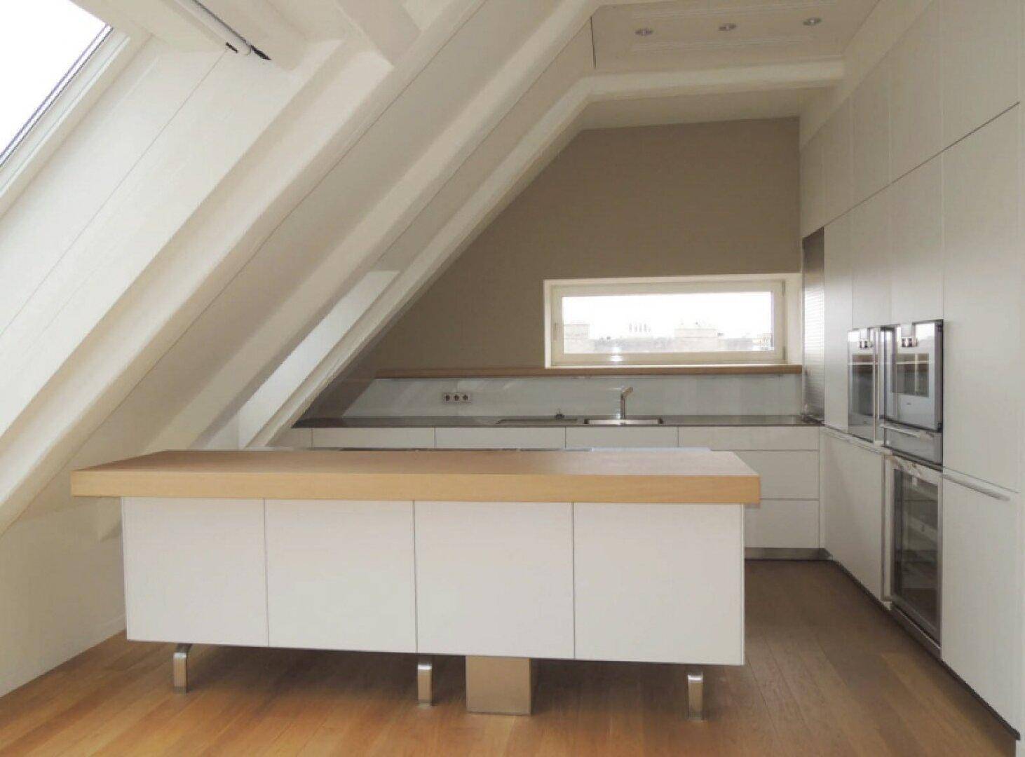 Moderne Küche im Dachgeschoss mit weißen Schränken, Holztheke und einem Fenster unter der Dachschräge.