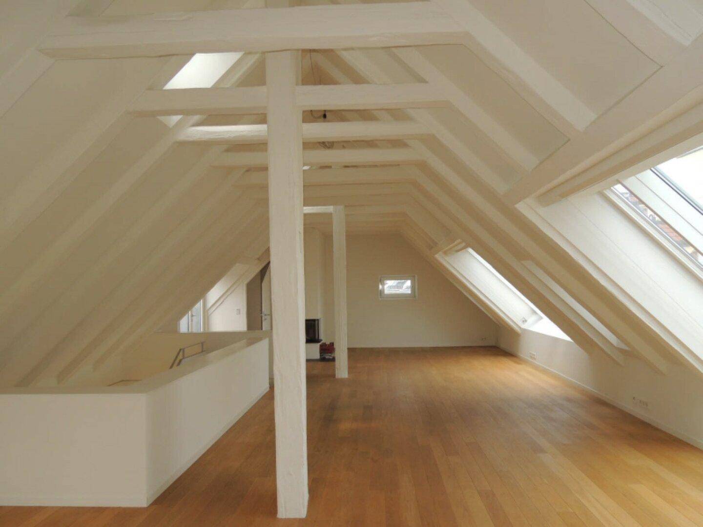 Weitläufiger Dachbodenraum mit freiliegenden Holzbalken, hellem Holzboden und mehreren Dachfenstern.