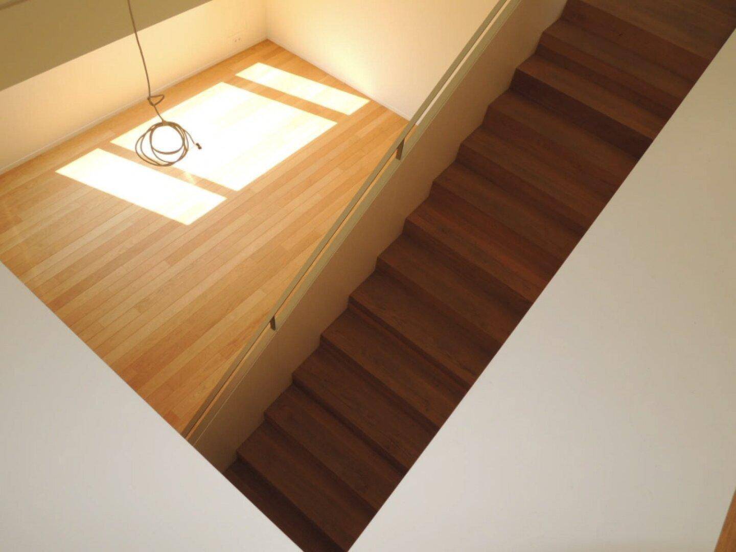 Blick von oben auf eine elegante Holztreppe, die zu einem hellen Raum mit Holzboden führt.