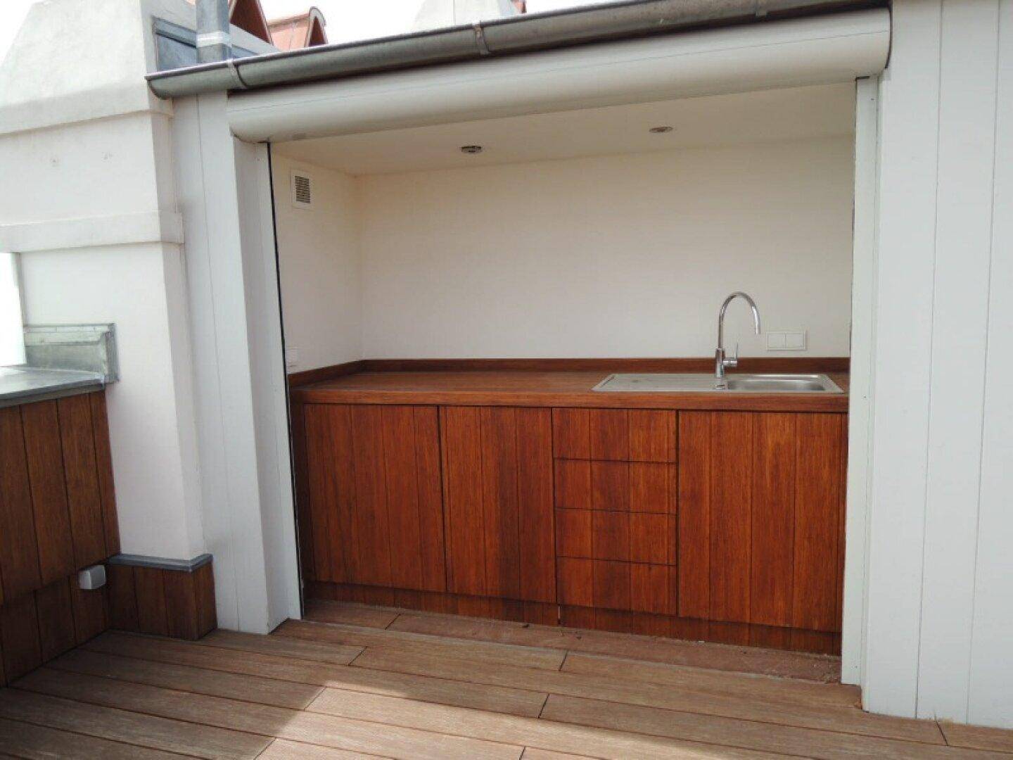 Praktische Außenküche auf einer Terrasse mit Holzschränken, Spüle und Arbeitsplatte.