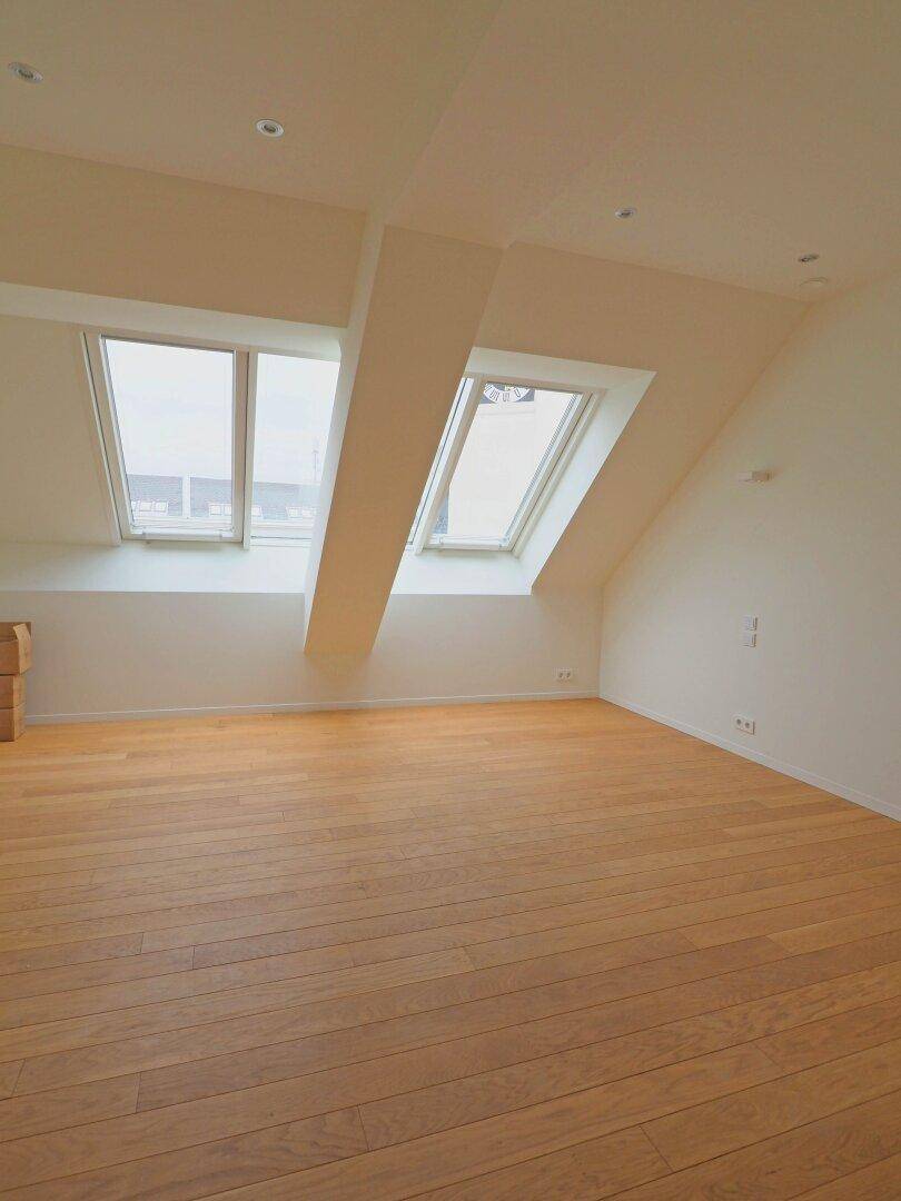 Helles Dachzimmer mit Holzboden, schrägen Wänden und großen Dachfenstern, die viel Licht hereinlassen.
