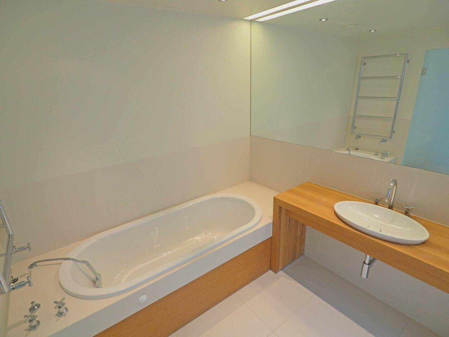 Elegantes Badezimmer mit eingebauter Badewanne, Einzelwaschbecken und einem großen Wandspiegel.