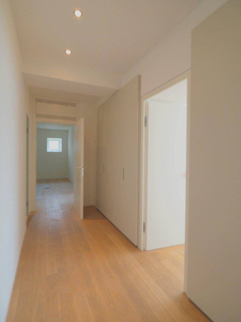Heller Flur mit Holzboden, weißen Wänden und integrierter Deckenbeleuchtung, führt zu weiteren Räumen.