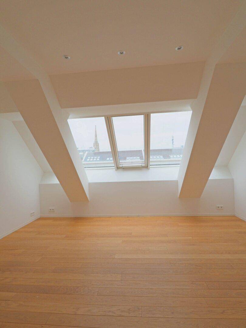 Lichtdurchflutetes Dachzimmer mit Holzboden und einer breiten Fensterfront in der Dachschräge.