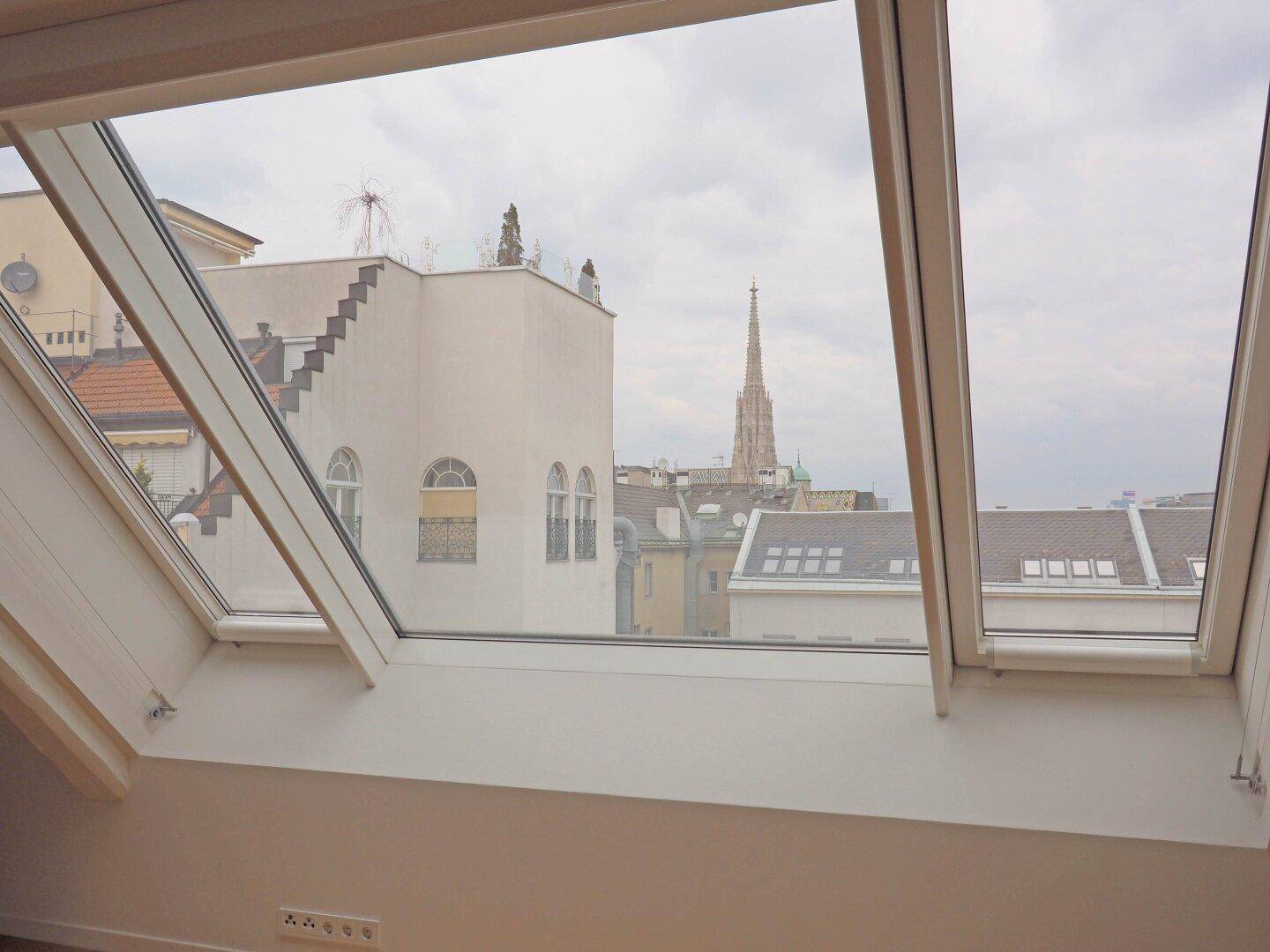 Ausblick aus einem Dachfenster auf die Stadtlandschaft mit historischer Kirchturmspitze.