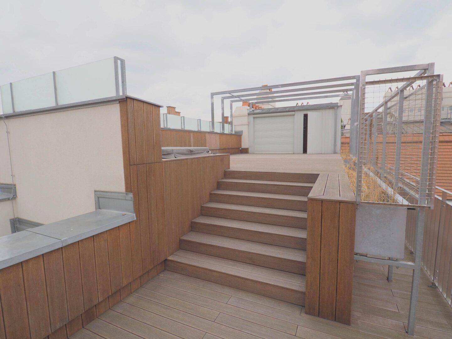 Geräumige Dachterrasse mit Holztreppe, Holzelementen und einem kleinen Abstellraum.