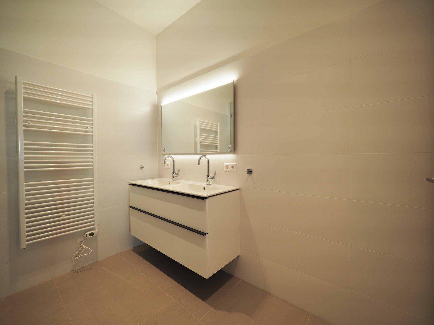 Modernes Badezimmer mit Doppelwaschbecken, beleuchtetem Spiegel und beheiztem Handtuchhalter.