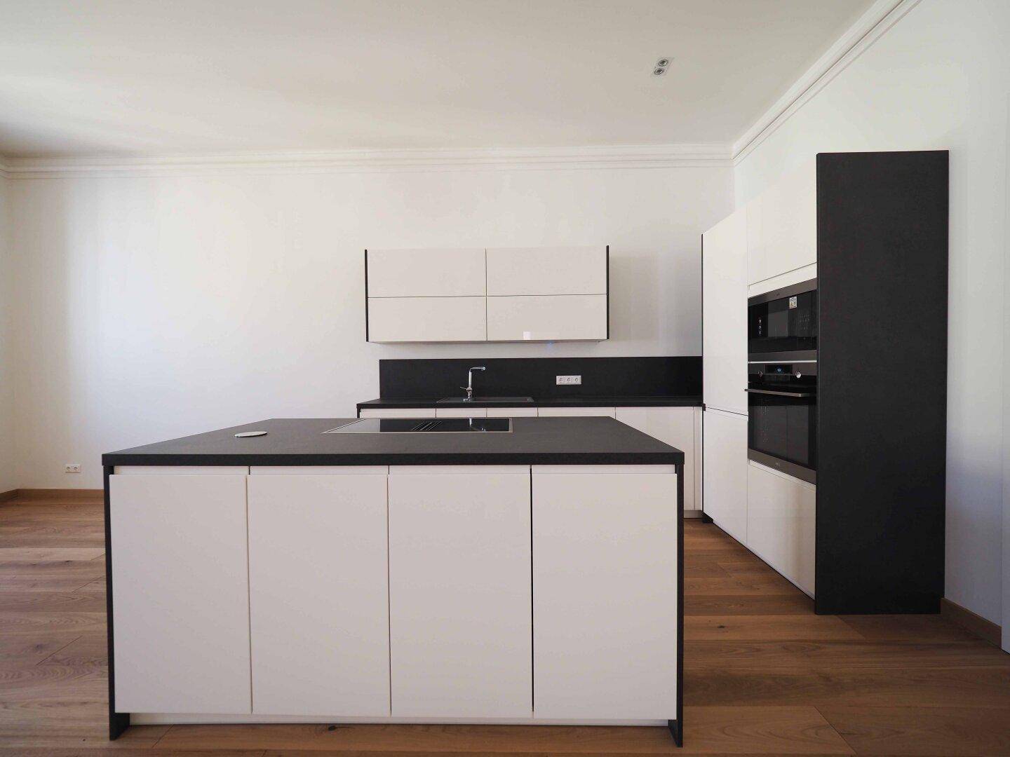 Elegante Küchenzeile mit dunklen Arbeitsplatten und integrierten Geräten, ergänzt durch eine Kochinsel.
