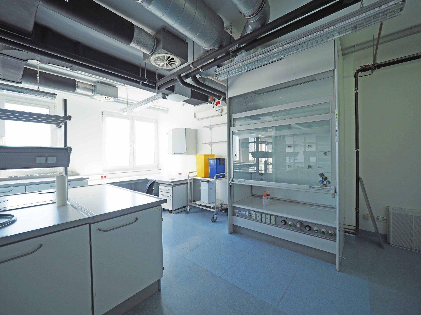 Laborraum mit Abzugshaube, weißen Schränken, blauem Boden und sichtbarer Lüftungsanlage an der Decke.