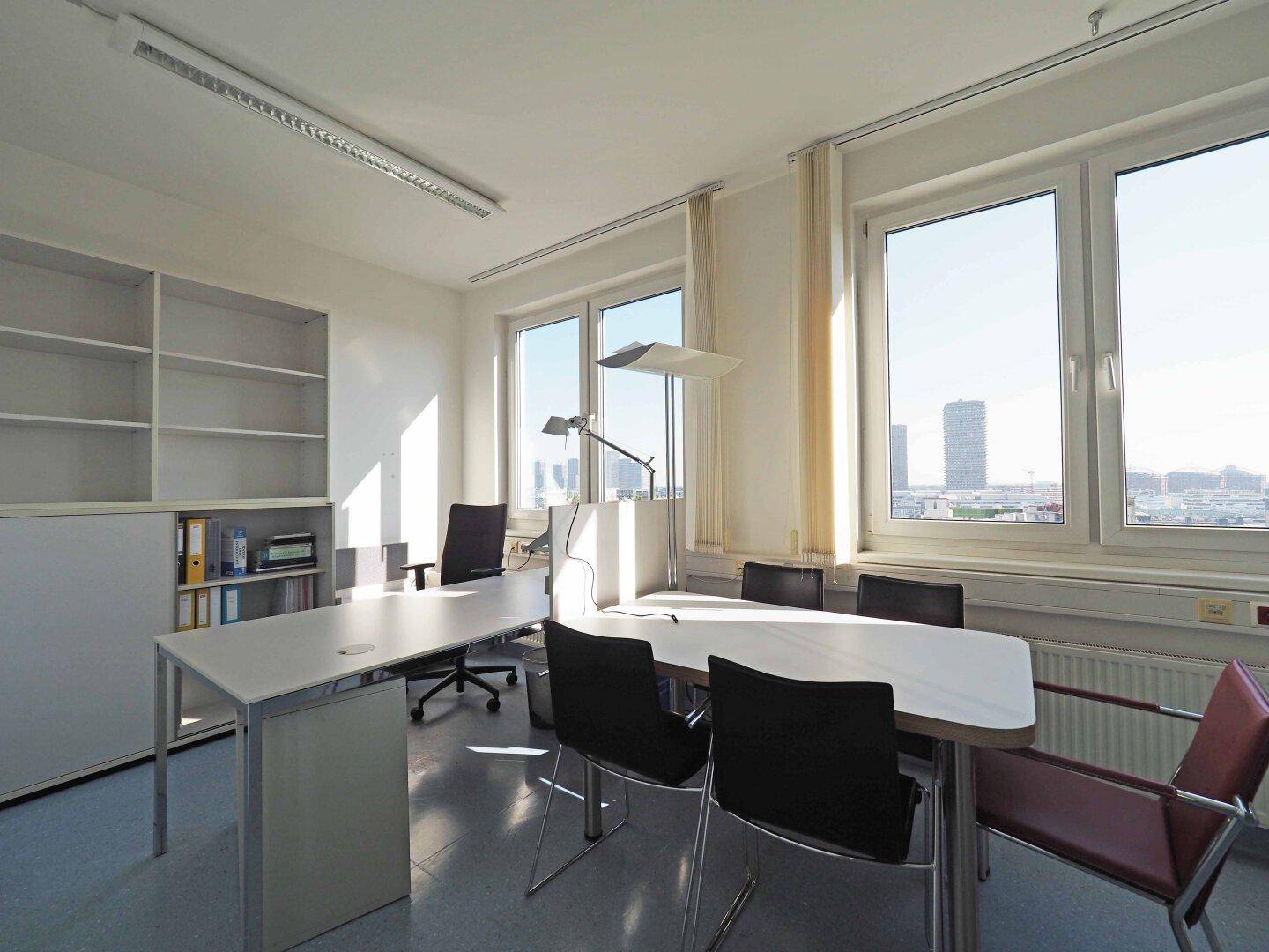 Helles Büro mit großem Fenster, das einen Stadtblick bietet, modernen Möbeln und weißen Regalsystemen.