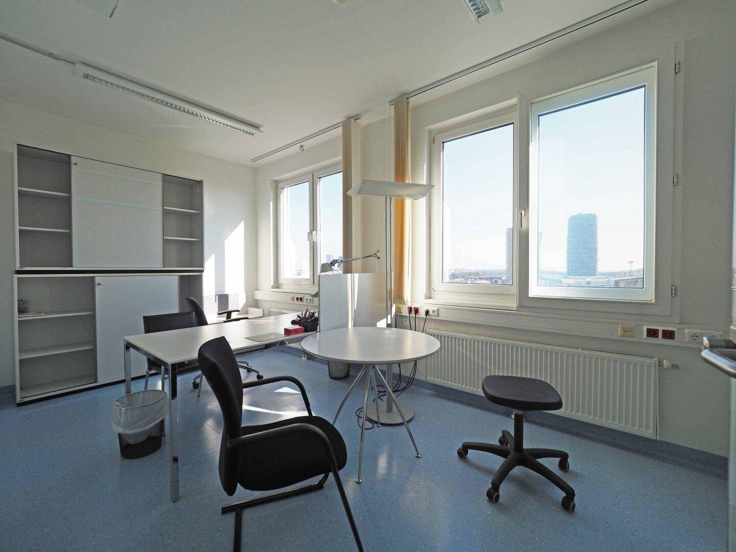 Büro mit blauem Boden, modernen Möbeln und großen Fenstern, die viel Tageslicht hereinlassen.