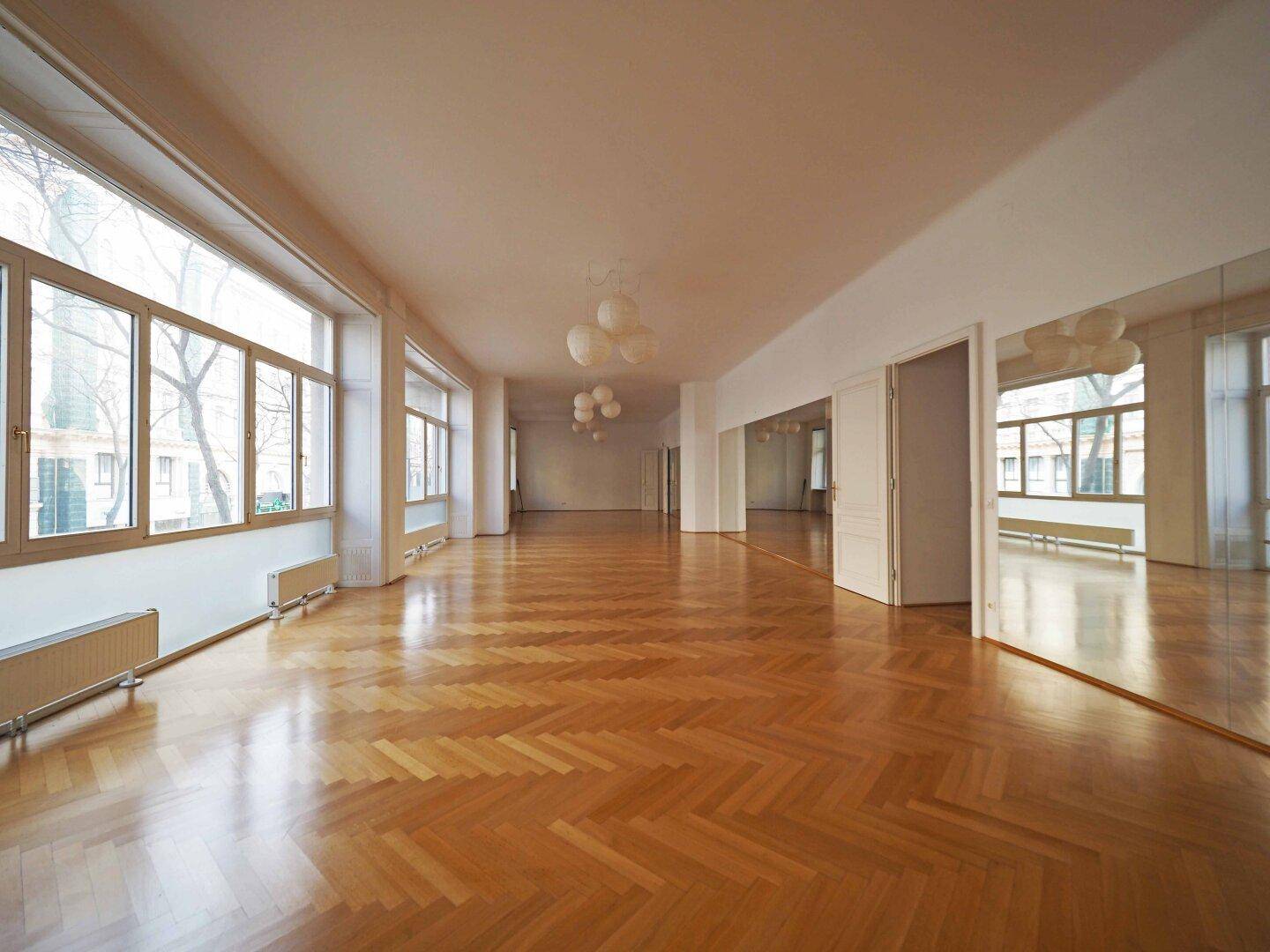 Geräumiger, heller Raum mit vielen Fenstern, Fischgrätparkett und hohen Decken.