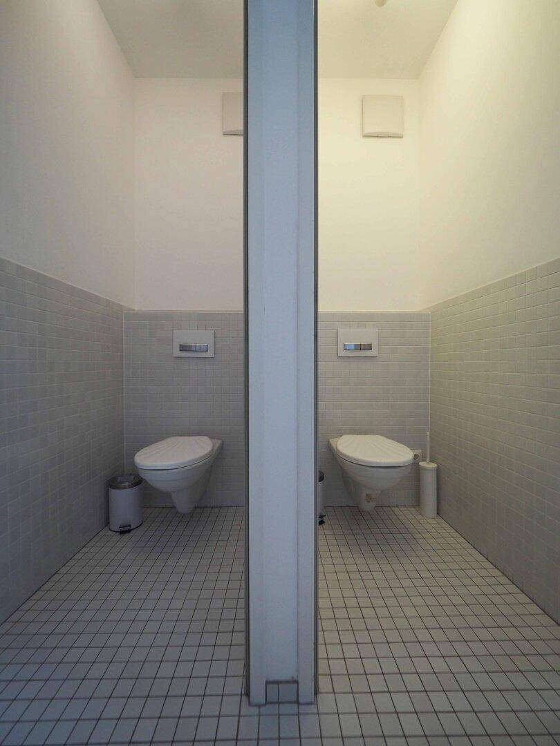 Zwei separate Toilettenkabinen mit Wand-WCs und weißen Fliesen.