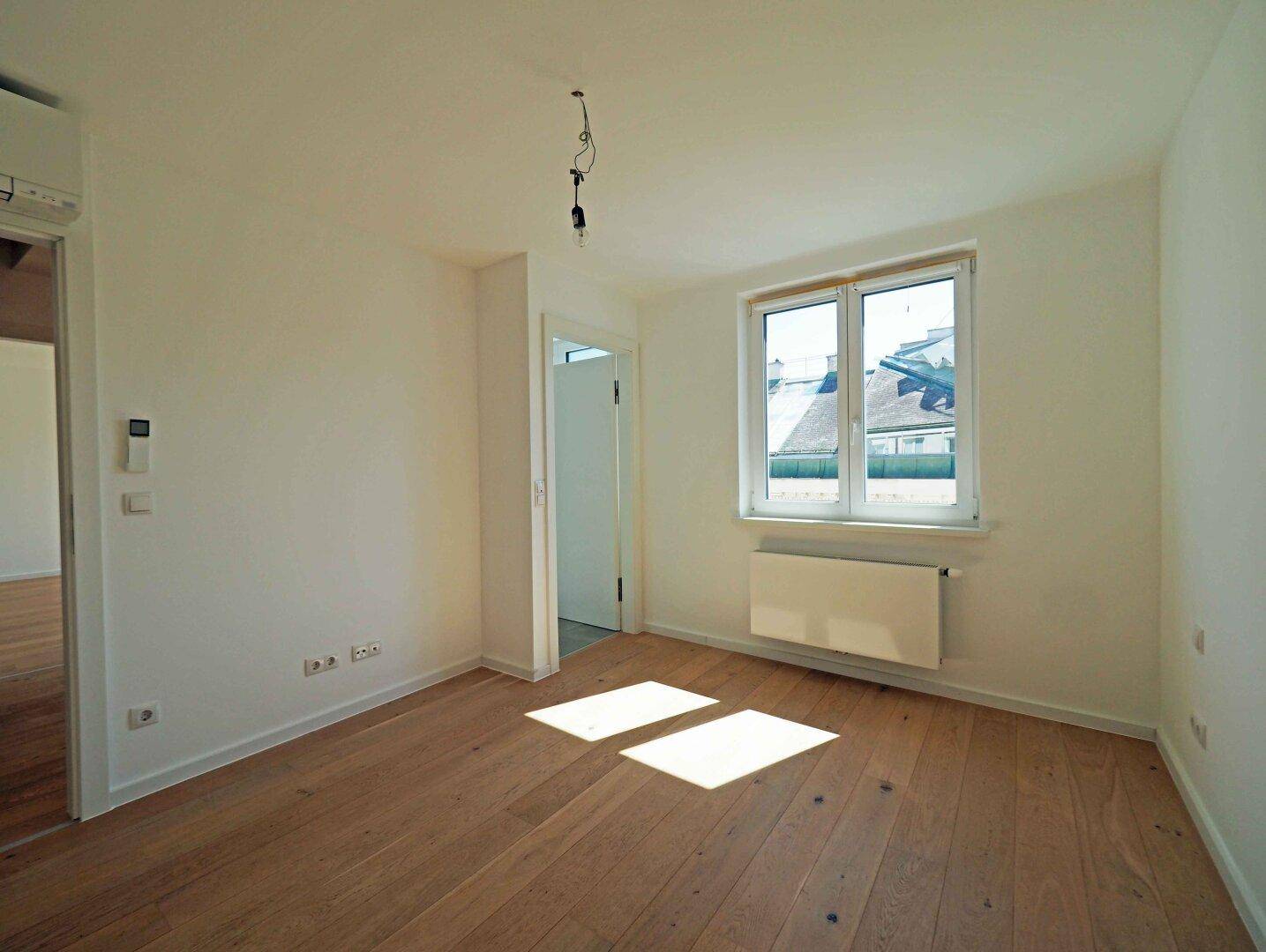 Helles Zimmer mit Holzboden und großem Fenster, ideal als Schlaf- oder Arbeitszimmer.