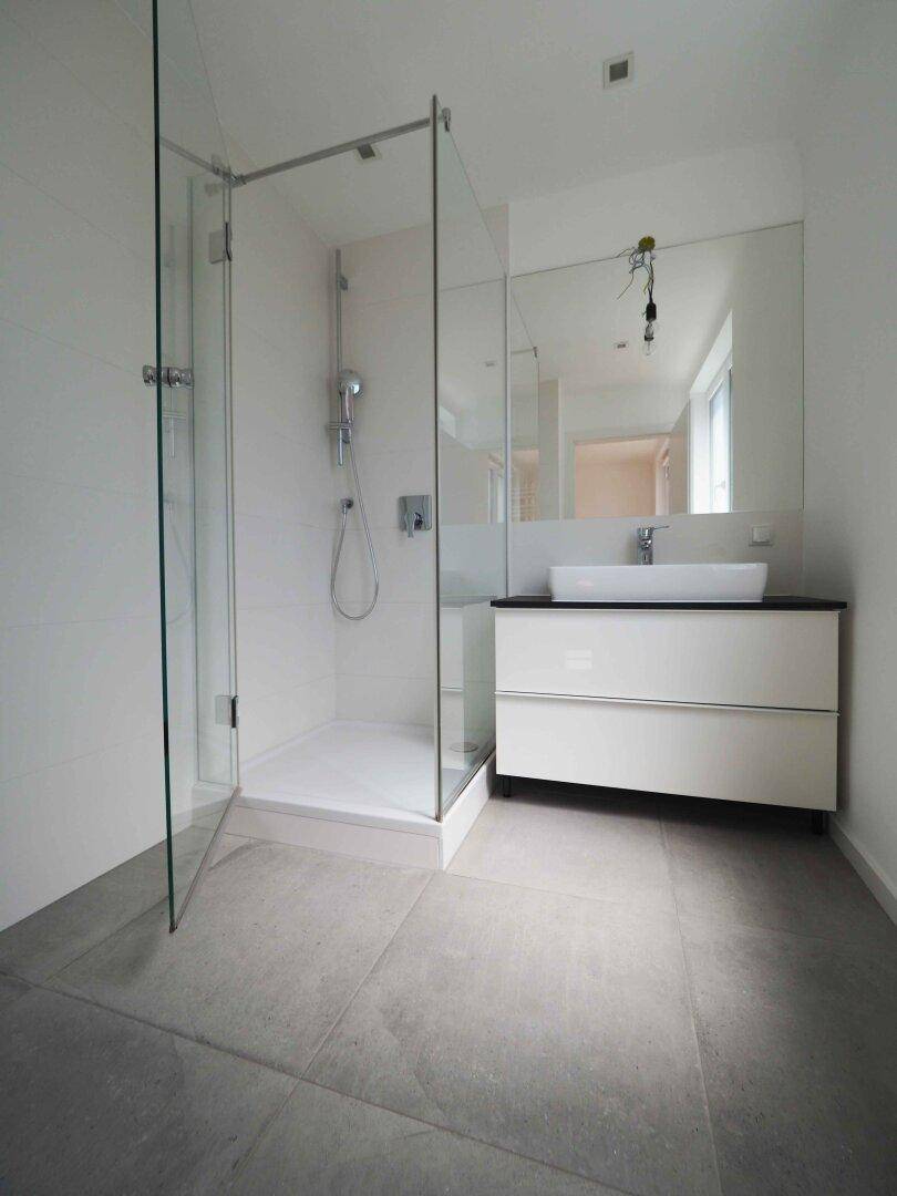 Modernes Badezimmer mit großer Glasdusche, Waschtisch und großem Spiegel.