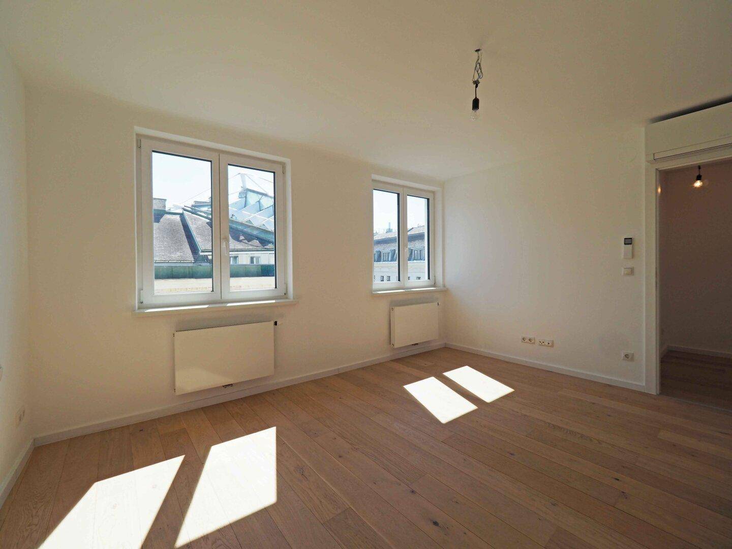 Geräumiges Zimmer mit Holzboden und zwei großen Fenstern, bietet viel Tageslicht.