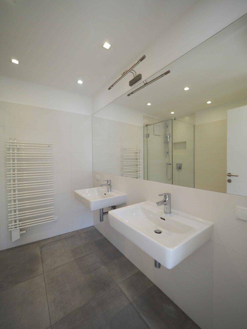Modernes Badezimmer mit Doppelwaschbecken, großem Spiegel und beheiztem Handtuchhalter.