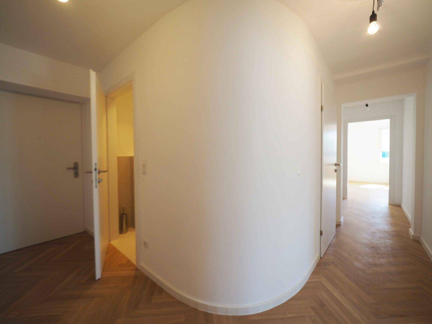 Heller Flur mit Fischgrätparkett und einer eleganten geschwungenen Wandführung.