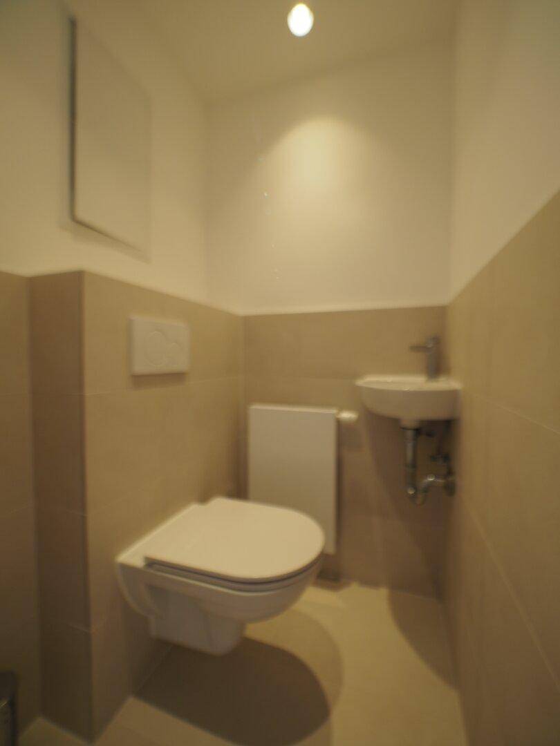 Kleines Gäste-WC mit beigefarbenen Fliesen, wandhängender Toilette und Waschbecken.