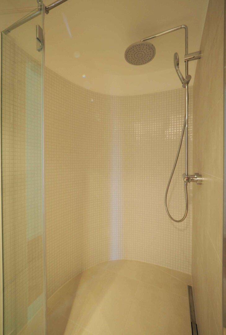 Moderne Dusche mit Mosaikfliesen und Regenduschkopf in einem hellen Badezimmer.