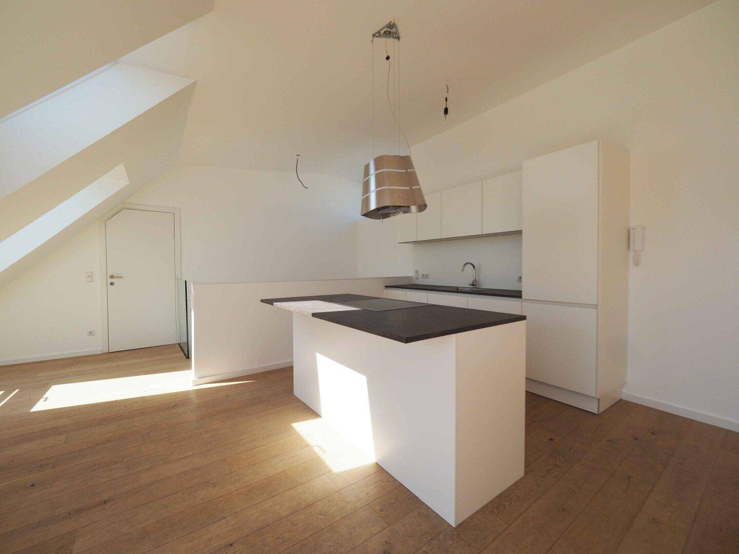 Moderne Einbauküche mit Kochinsel, weißen Schränken und Holzboden im Dachgeschoss.