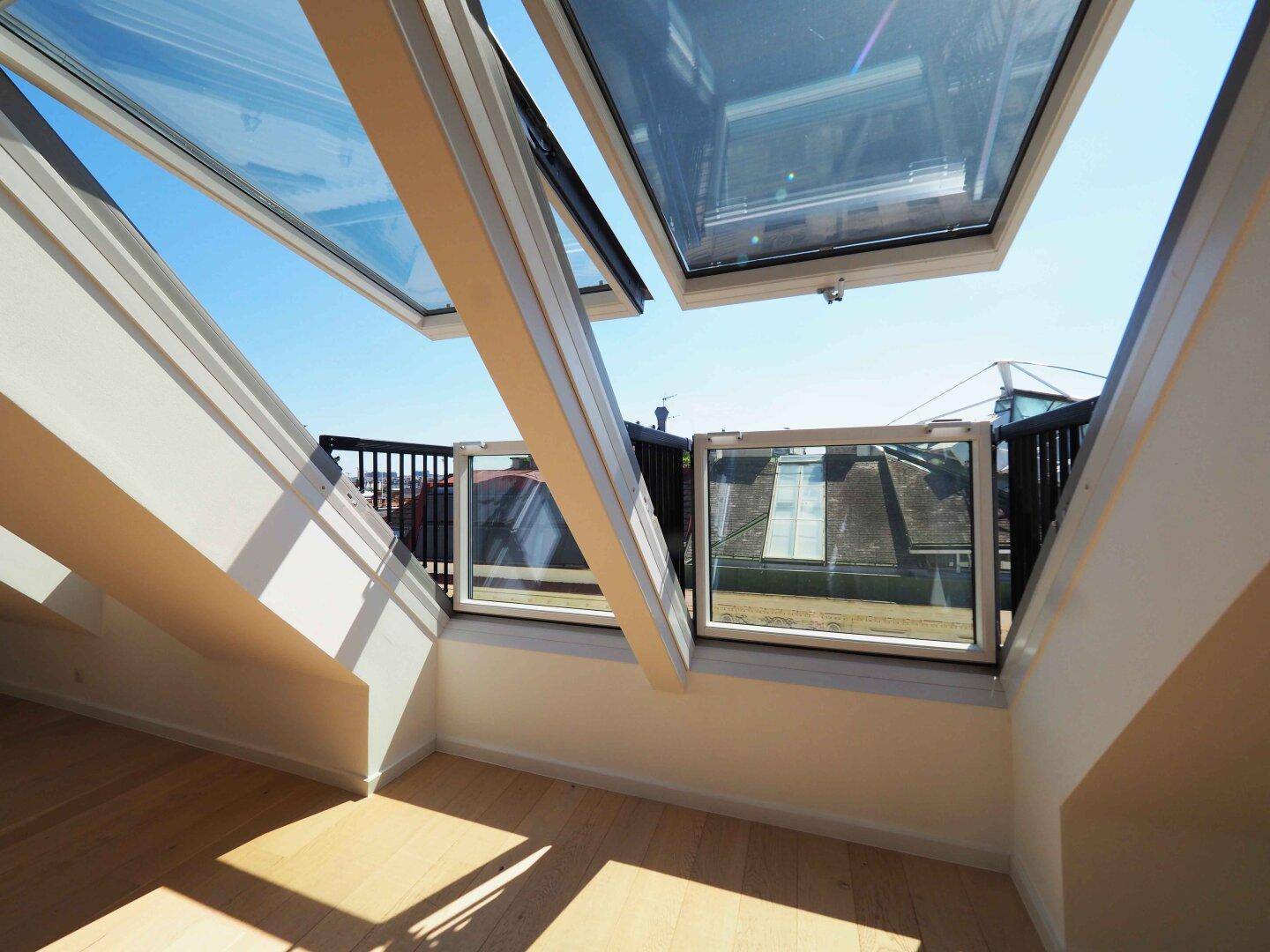 Helles Dachgeschosszimmer mit innovativen Dachfenstern, die sich zu einem kleinen Balkon öffnen.