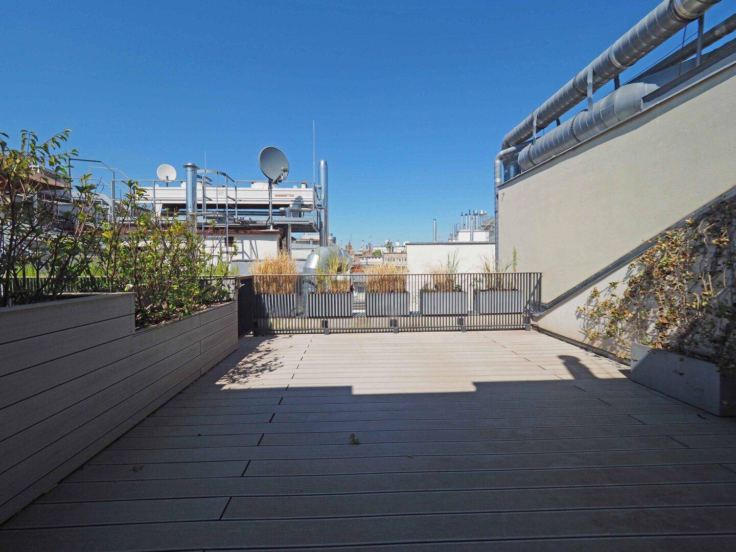 Geräumige Dachterrasse mit Holzbelag und Pflanzen, bietet viel Platz im Freien.