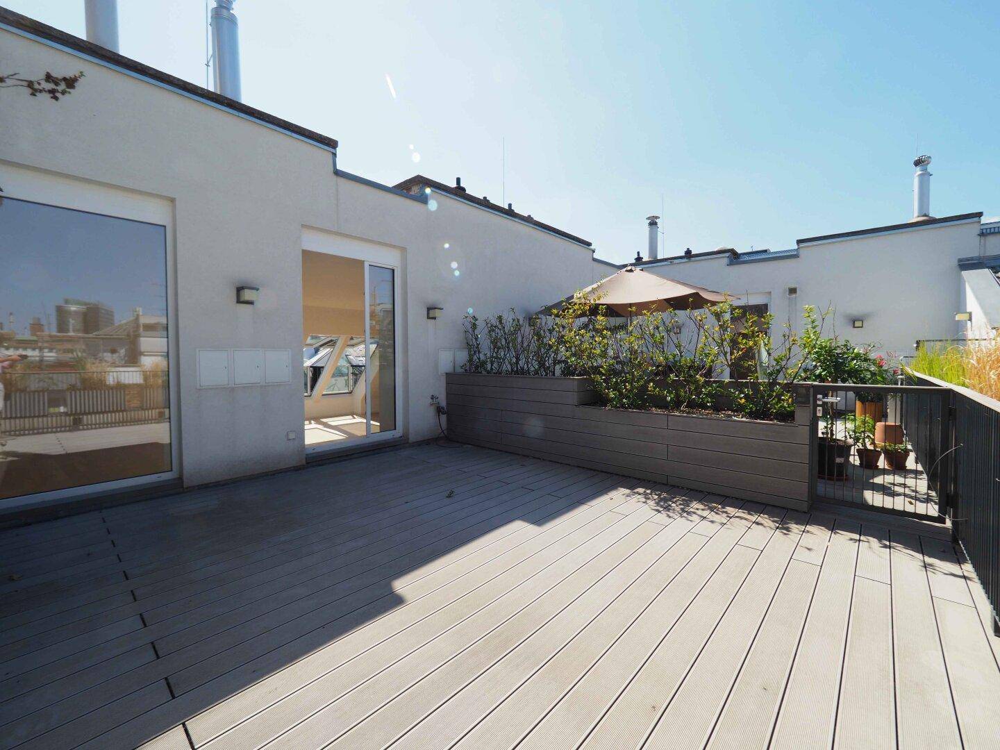 Sonnige Dachterrasse mit Holzbelag, Pflanzen und Sonnenschirm, ideal zum Entspannen.