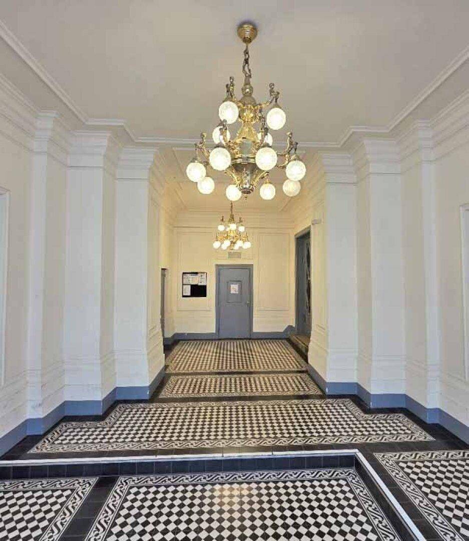 Eleganter Flur mit Schachbrettmuster-Fliesenboden und opulenten Kronleuchtern, der zu weiteren Räumen führt.