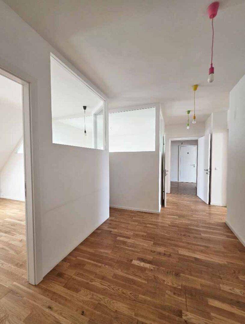 Heller Flur mit Holzparkettboden und modernen, farbigen Hängelampen, der zu mehreren Zimmern führt.